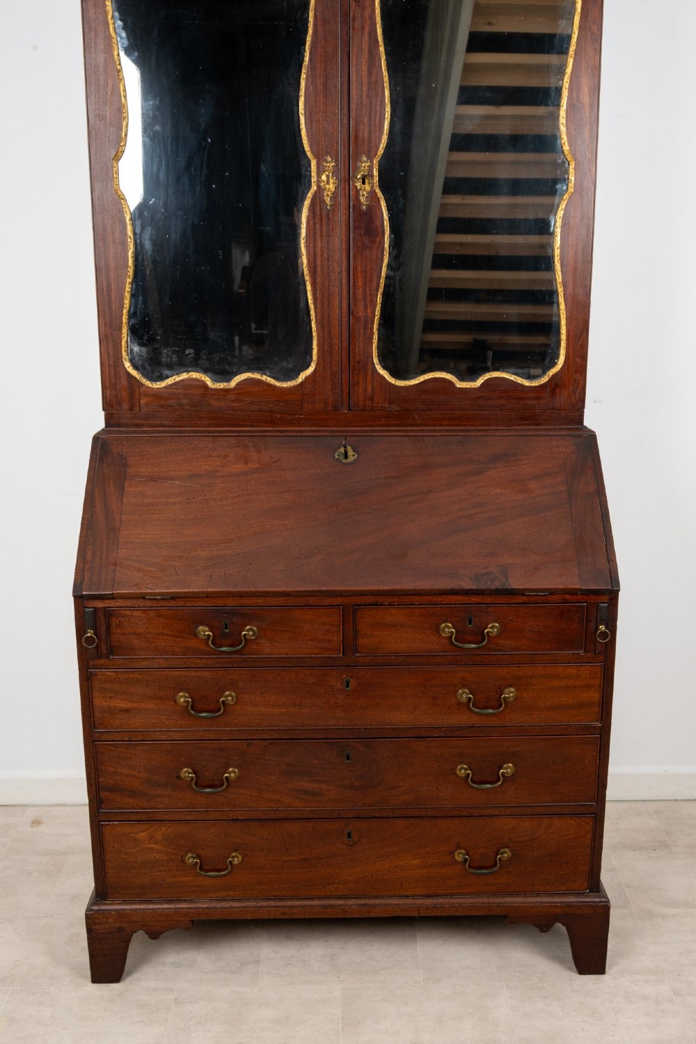 An eighteenth-century mahogany bureau bookcase featuring shaped mirrored double doors on the upper cabinet, a slant-front desk midsection, and four graduated drawers below with brass drop handles. View V