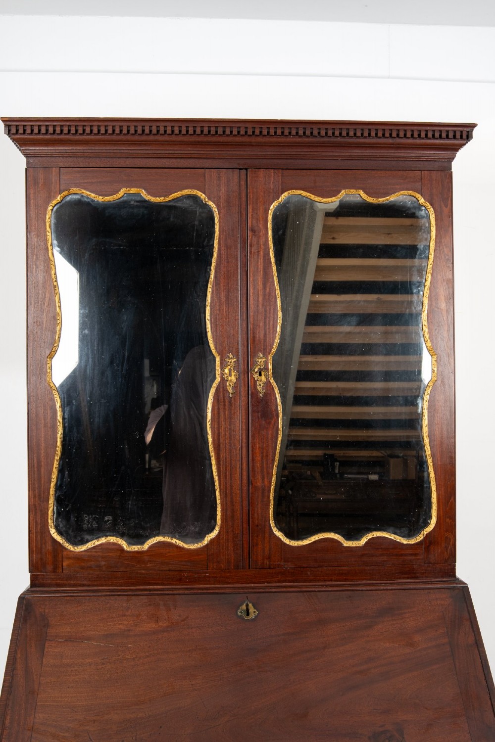 An eighteenth-century mahogany bureau bookcase featuring shaped mirrored double doors on the upper cabinet, a slant-front desk midsection, and four graduated drawers below with brass drop handles. View VI