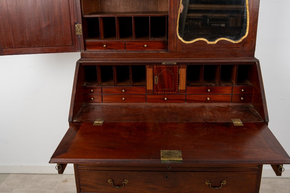An eighteenth-century mahogany bureau bookcase featuring shaped mirrored double doors on the upper cabinet, a slant-front desk midsection, and four graduated drawers below with brass drop handles. View VIII