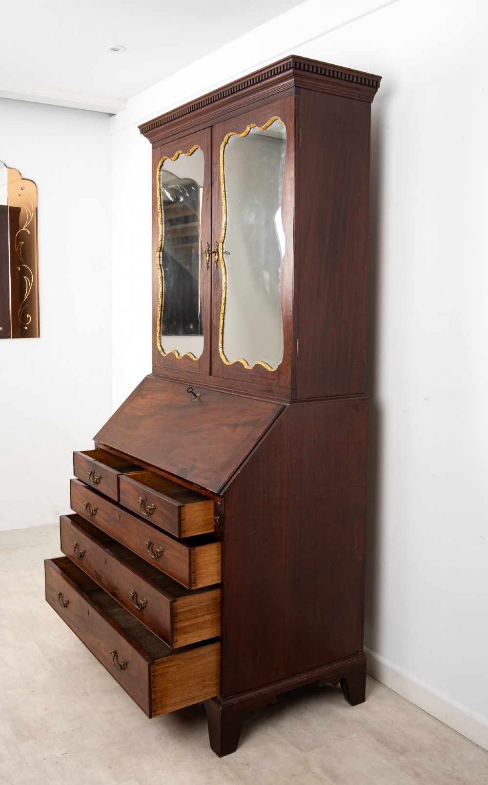 An eighteenth-century mahogany bureau bookcase featuring shaped mirrored double doors on the upper cabinet, a slant-front desk midsection, and four graduated drawers below with brass drop handles. View IX