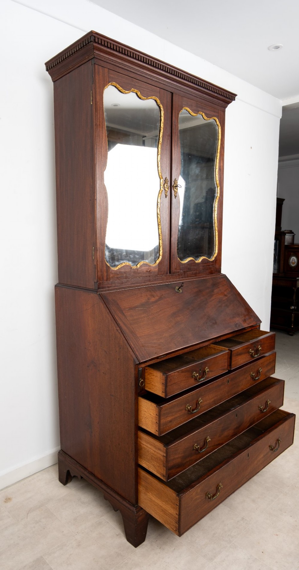 An eighteenth-century mahogany bureau bookcase featuring shaped mirrored double doors on the upper cabinet, a slant-front desk midsection, and four graduated drawers below with brass drop handles. View X