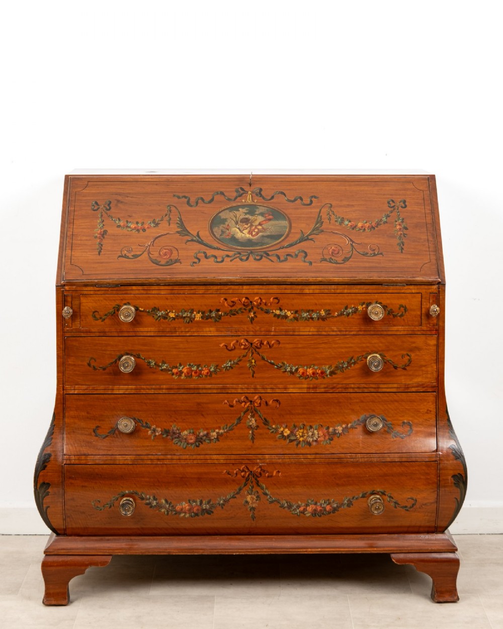 An Edwardian satinwood slant-front bureau with hand-painted floral swags, ribbon garlands, four drawers, and bracket feet.