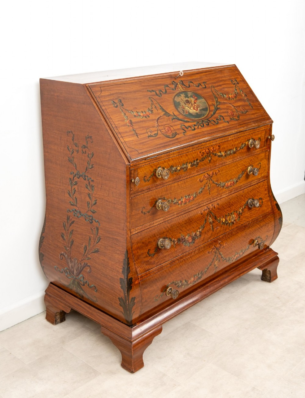 An Edwardian satinwood slant-front bureau with hand-painted floral swags, ribbon garlands, four drawers, and bracket feet. View V