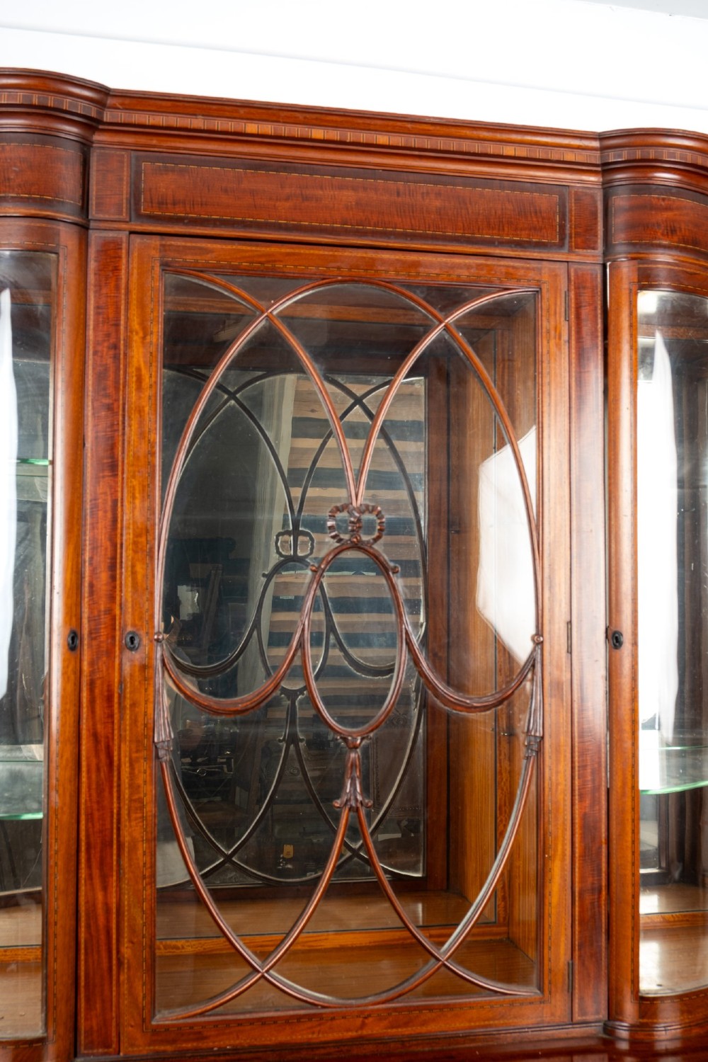 An Edwardian mahogany serpentine display cabinet featuring a central glazed door with geometric astragal glazing, glass side panels, and a hand-painted floral landscape panel on the lower central door. View V