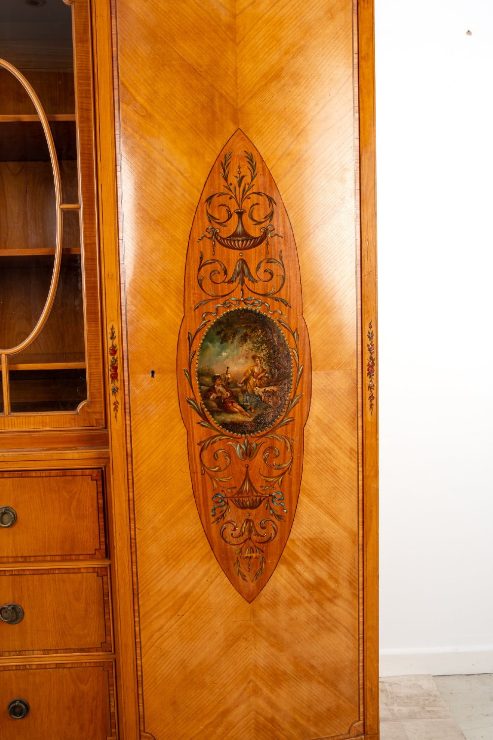 An Edwardian satinwood breakfront compactum wardrobe featuring central glazed doors, three drawers, and flanking bow-front cupboards decorated with hand-painted oval medallions. View II
