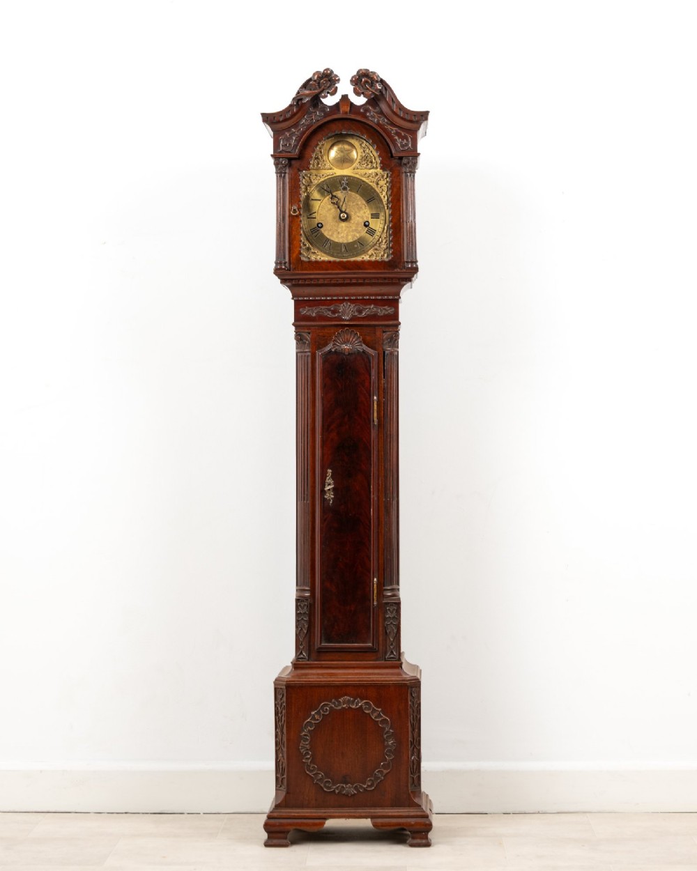 An Edwardian mahogany grandmother clock with a carved swan neck pediment, a brass dial with Roman numerals, and a slim waist door.