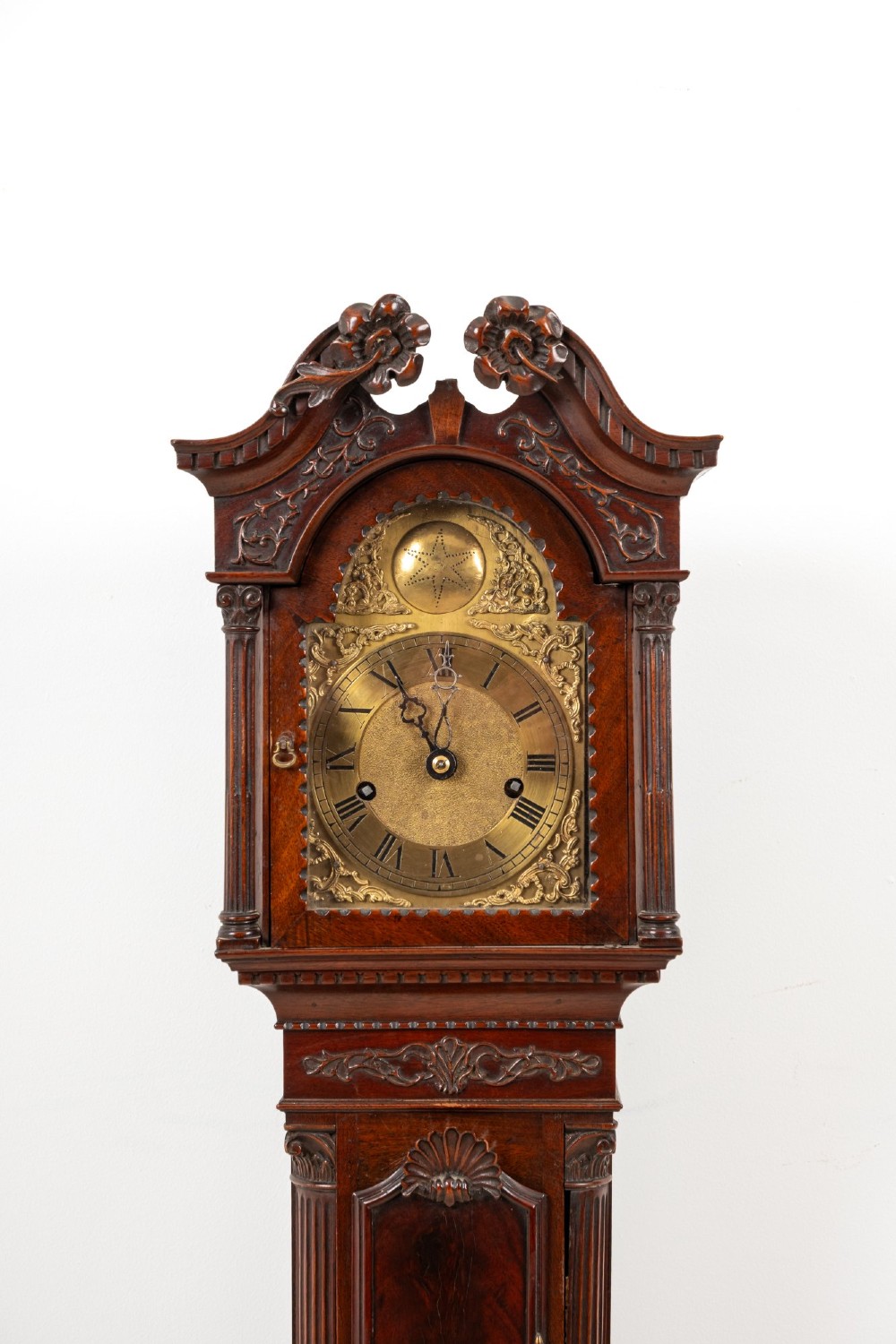 An Edwardian mahogany grandmother clock with a carved swan neck pediment, a brass dial with Roman numerals, and a slim waist door. View IV