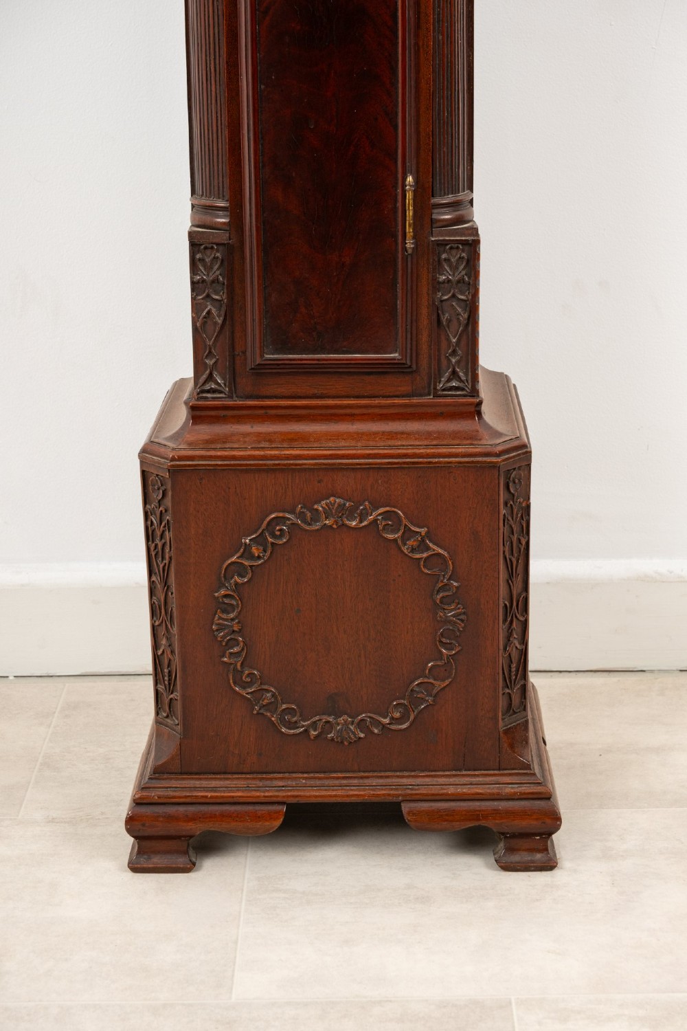 An Edwardian mahogany grandmother clock with a carved swan neck pediment, a brass dial with Roman numerals, and a slim waist door. View V