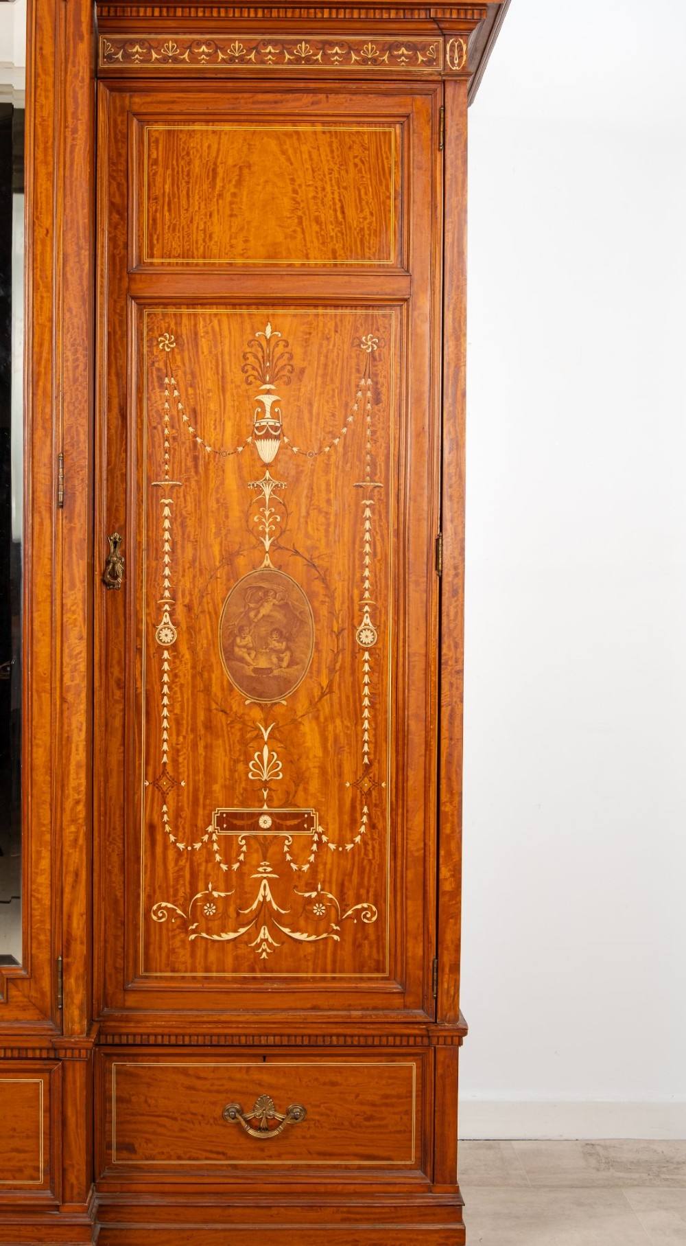 An Edwardian satinwood triple wardrobe with a stepped cornice, central mirror door, side doors decorated with painted classical urns, and three lower drawers. View III