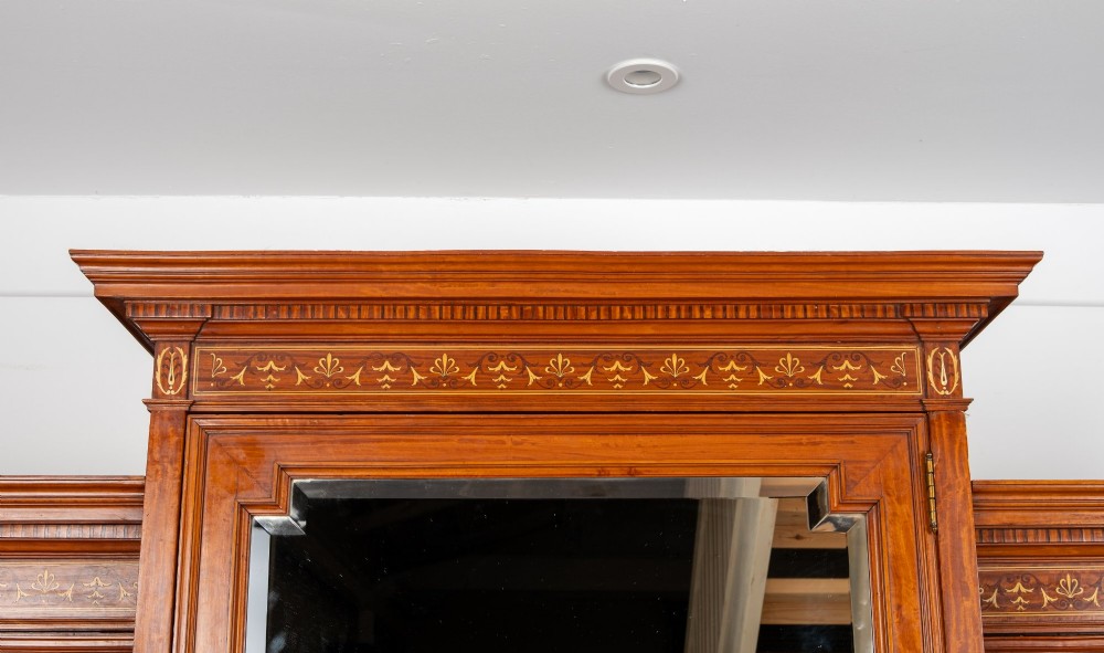An Edwardian satinwood triple wardrobe with a stepped cornice, central mirror door, side doors decorated with painted classical urns, and three lower drawers. View VII