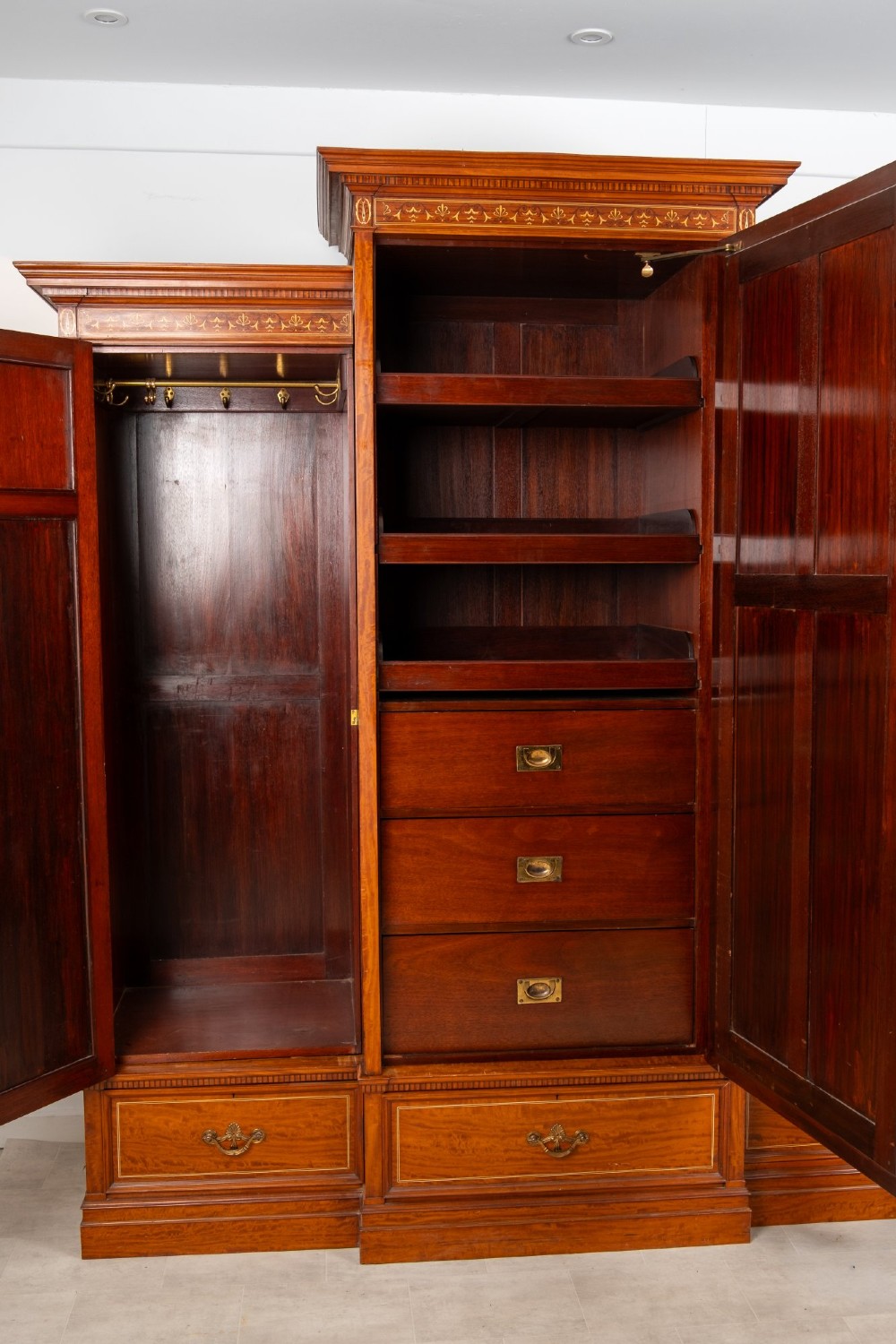 An Edwardian satinwood triple wardrobe with a stepped cornice, central mirror door, side doors decorated with painted classical urns, and three lower drawers. View VIII