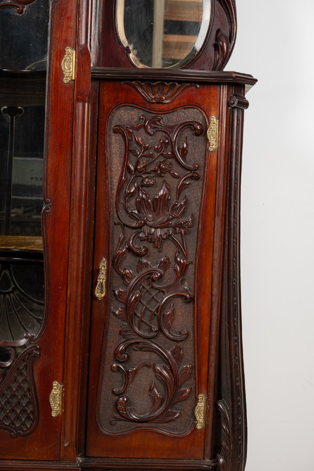 Late Victorian mahogany display cabinet featuring a central glazed door with intricate carved tracery, flanking carved timber doors, side mirror panels, and shaped cresting. View V