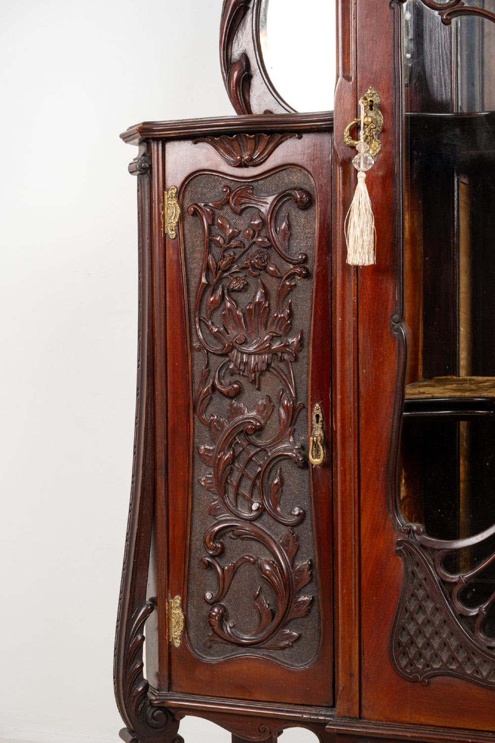 Late Victorian mahogany display cabinet featuring a central glazed door with intricate carved tracery, flanking carved timber doors, side mirror panels, and shaped cresting. View VI