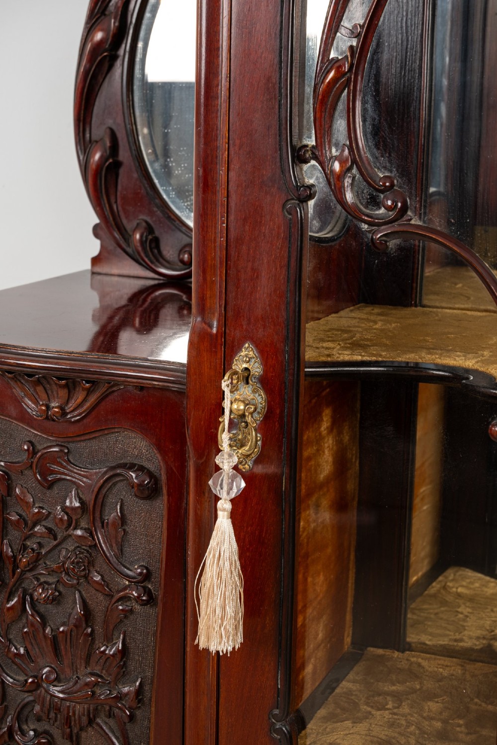 Late Victorian mahogany display cabinet featuring a central glazed door with intricate carved tracery, flanking carved timber doors, side mirror panels, and shaped cresting. View VII