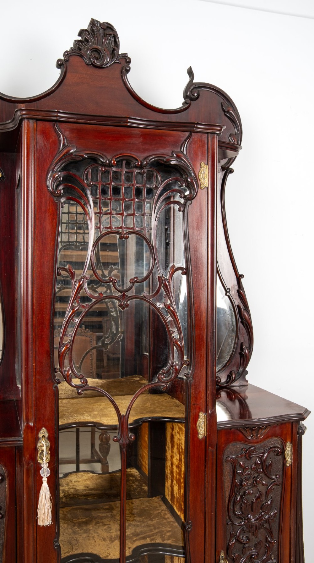 Late Victorian mahogany display cabinet featuring a central glazed door with intricate carved tracery, flanking carved timber doors, side mirror panels, and shaped cresting. View VIII