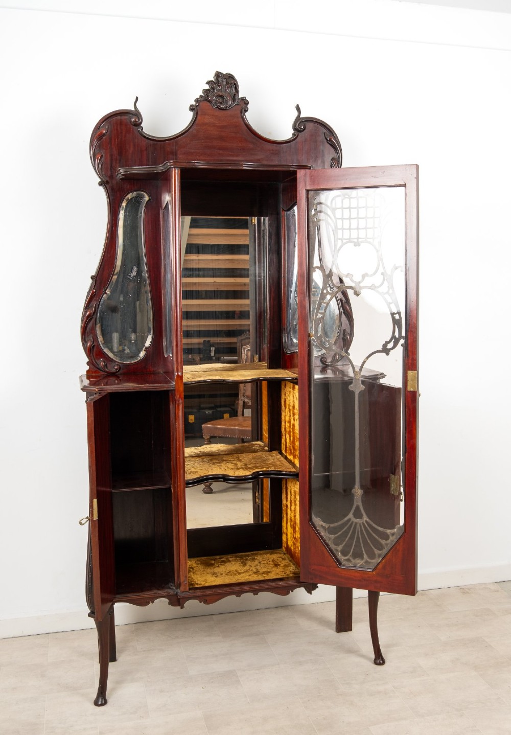 Late Victorian mahogany display cabinet featuring a central glazed door with intricate carved tracery, flanking carved timber doors, side mirror panels, and shaped cresting. View IX