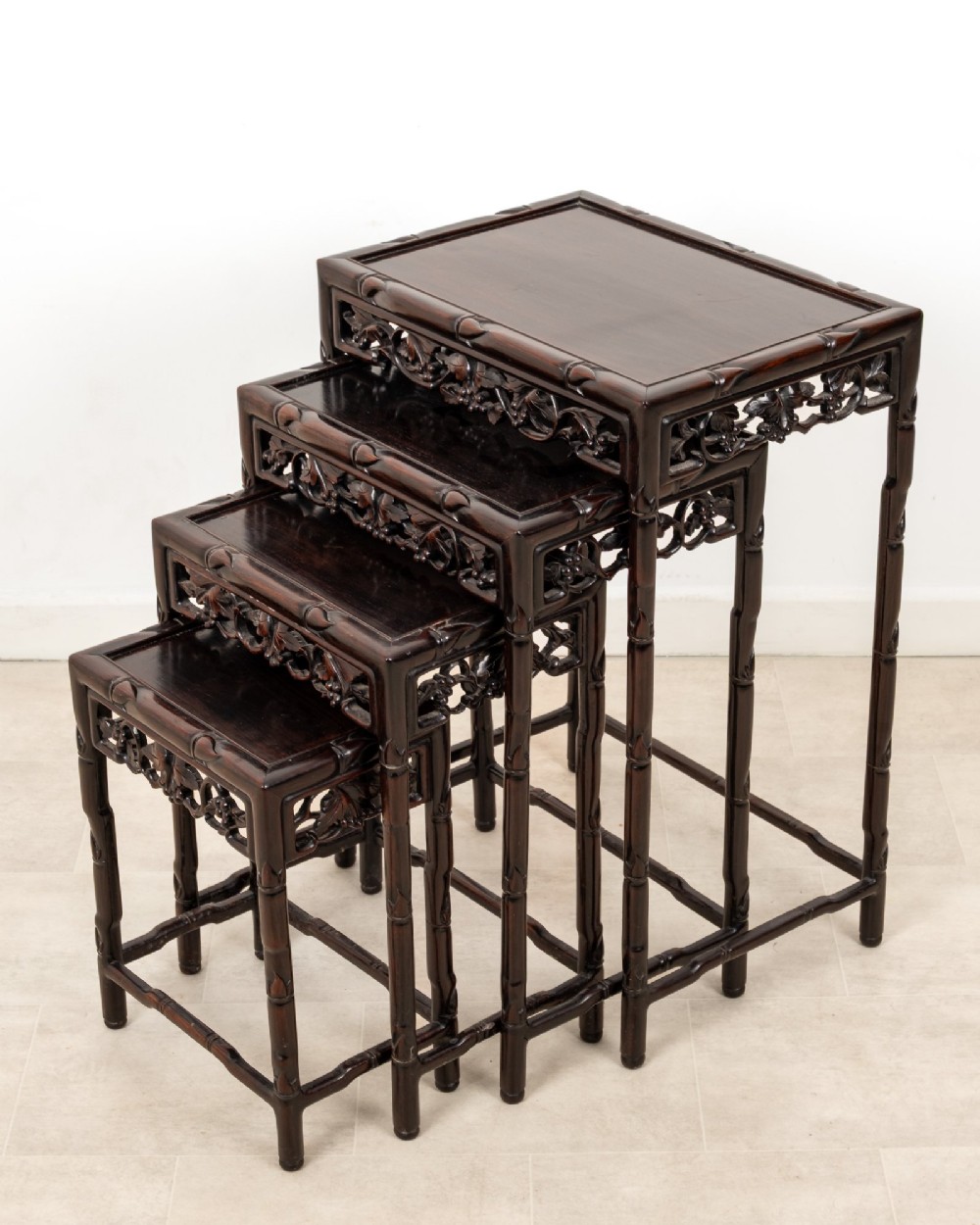 A set of four dark hardwood nested side tables featuring carved faux bamboo legs and openwork carved aprons, shown arranged in a graduated stepped stack. View II