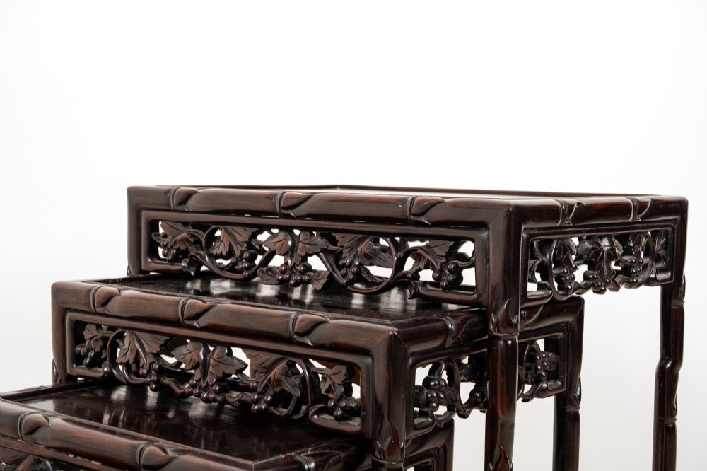 A set of four dark hardwood nested side tables featuring carved faux bamboo legs and openwork carved aprons, shown arranged in a graduated stepped stack. View III