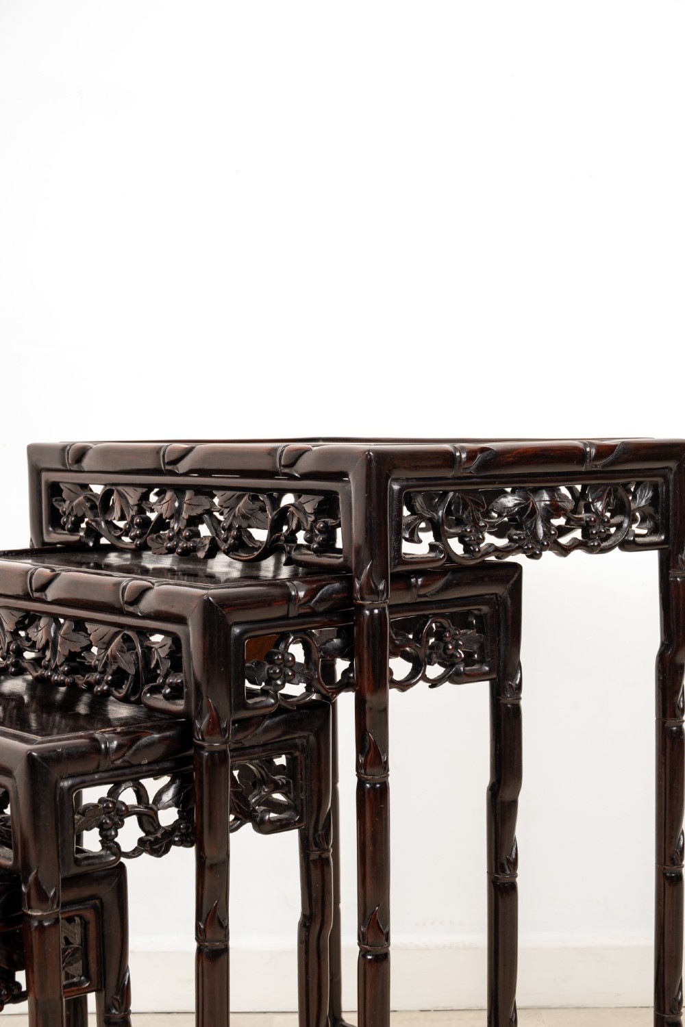 A set of four dark hardwood nested side tables featuring carved faux bamboo legs and openwork carved aprons, shown arranged in a graduated stepped stack. View V