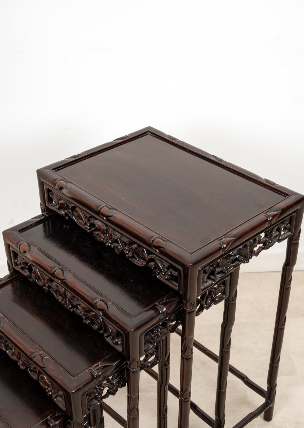 A set of four dark hardwood nested side tables featuring carved faux bamboo legs and openwork carved aprons, shown arranged in a graduated stepped stack. View VI