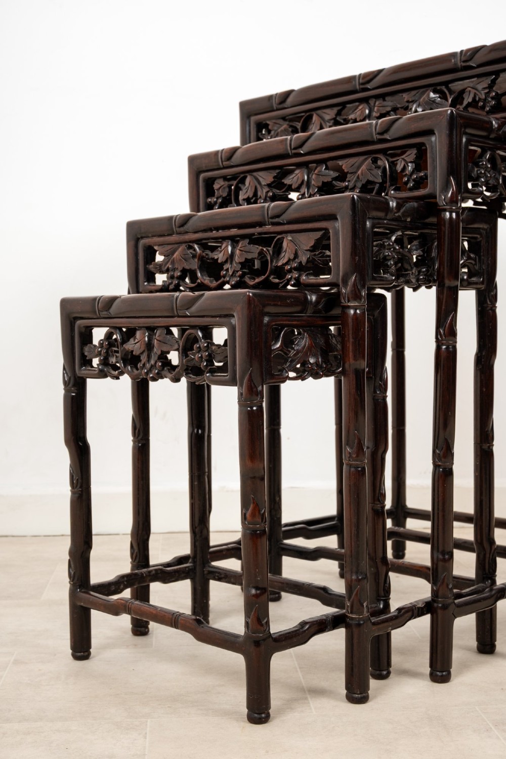 A set of four dark hardwood nested side tables featuring carved faux bamboo legs and openwork carved aprons, shown arranged in a graduated stepped stack. View VII