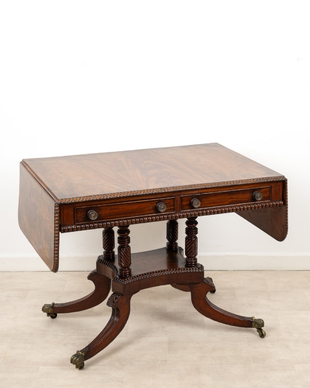 A 19th-century mahogany drop-leaf sofa table with four spiral-turned column supports, frieze drawers, and splayed legs on brass castors.
