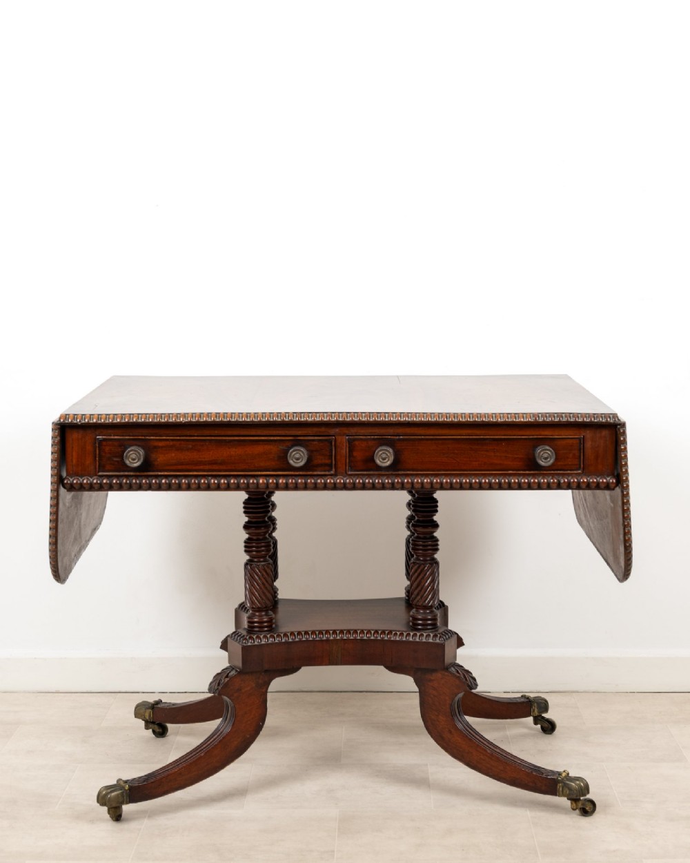 A 19th-century mahogany drop-leaf sofa table with four spiral-turned column supports, frieze drawers, and splayed legs on brass castors. View II
