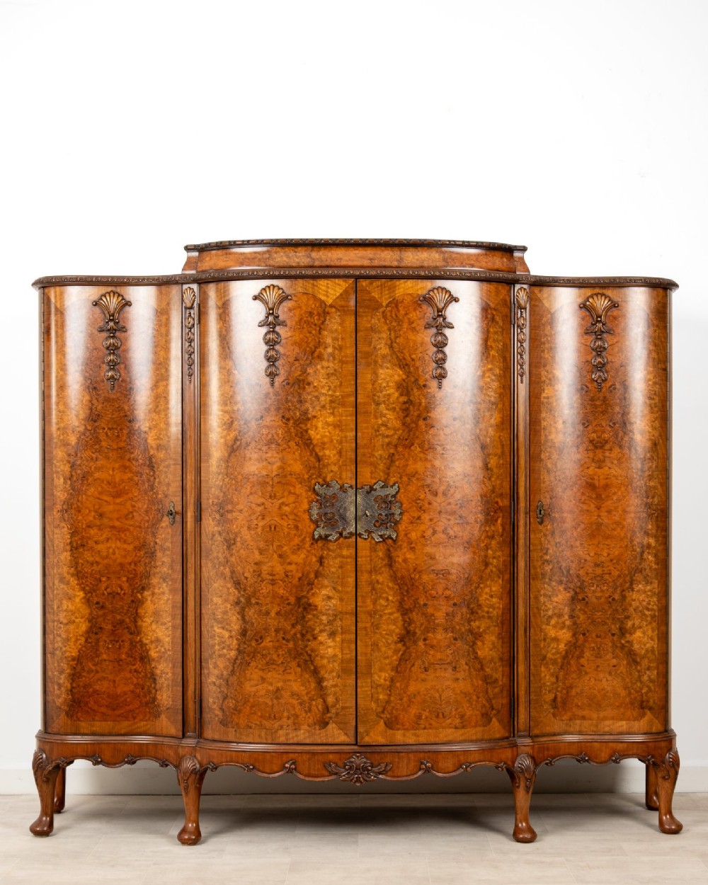 A 1930s burr walnut cocktail cabinet with book-matched veneers, carved shell motifs, brass hinges, and cabriole legs.