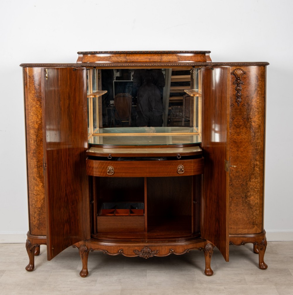 A 1930s burr walnut cocktail cabinet with book-matched veneers, carved shell motifs, brass hinges, and cabriole legs. View IX
