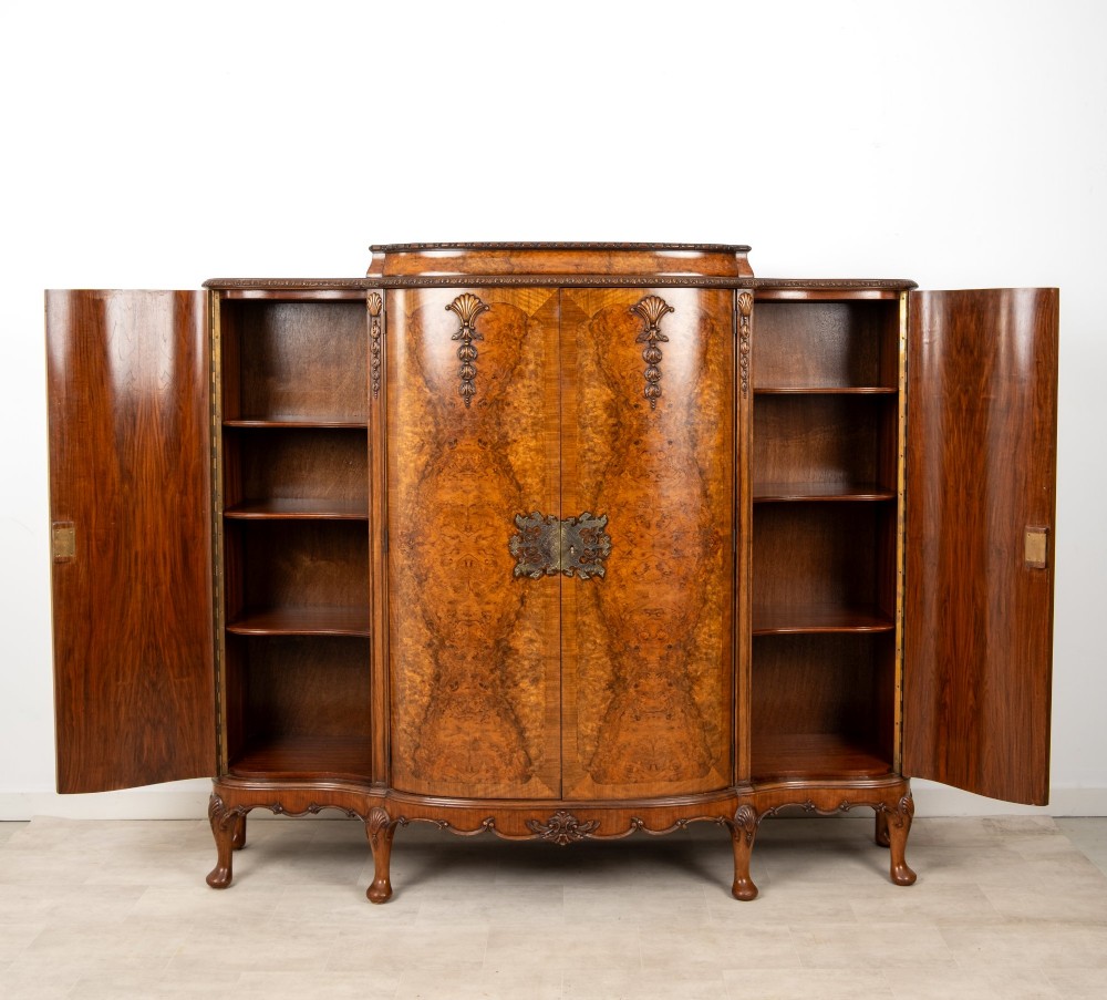 A 1930s burr walnut cocktail cabinet with book-matched veneers, carved shell motifs, brass hinges, and cabriole legs. View X