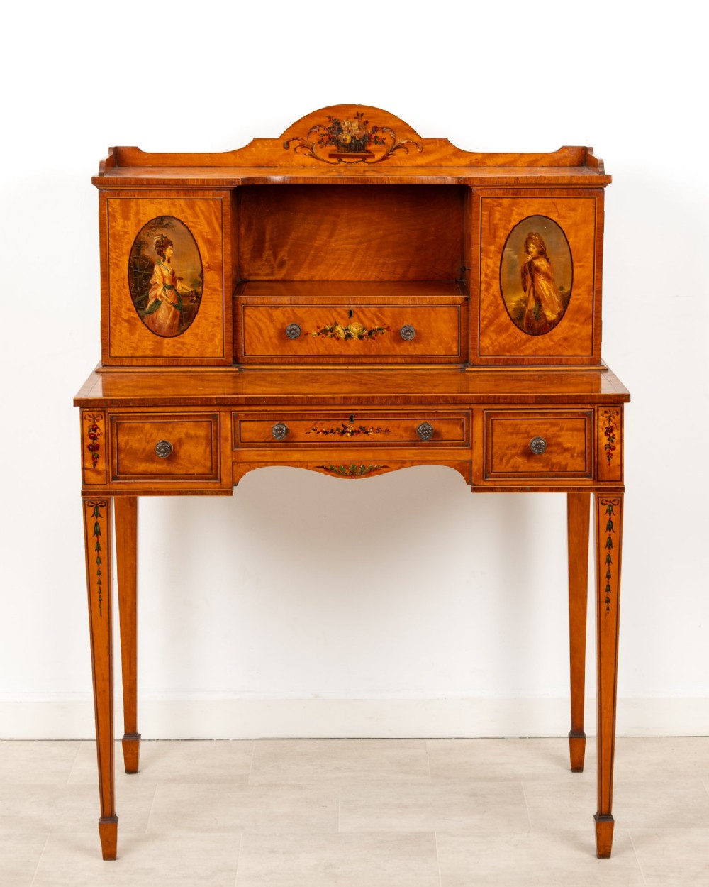 An Edwardian hand-painted satinwood writing desk featuring a raised central cupboard superstructure decorated with painted oval portraits, floral swags, and square tapered legs. View III