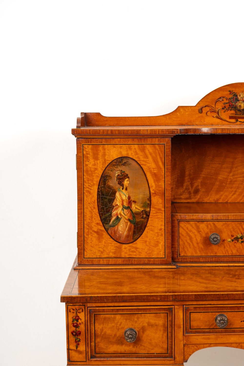 An Edwardian hand-painted satinwood writing desk featuring a raised central cupboard superstructure decorated with painted oval portraits, floral swags, and square tapered legs. View VI