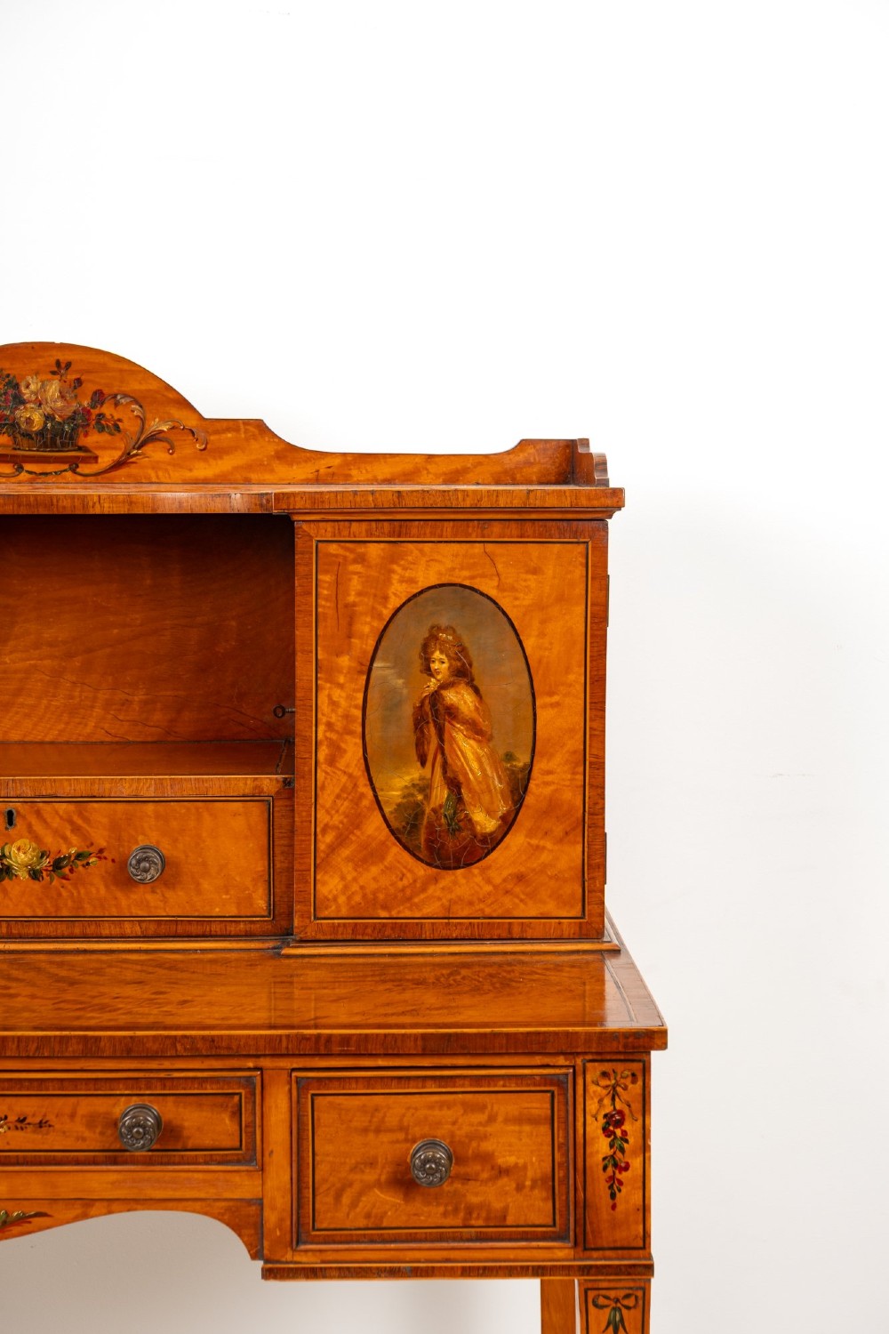 An Edwardian hand-painted satinwood writing desk featuring a raised central cupboard superstructure decorated with painted oval portraits, floral swags, and square tapered legs. View VII