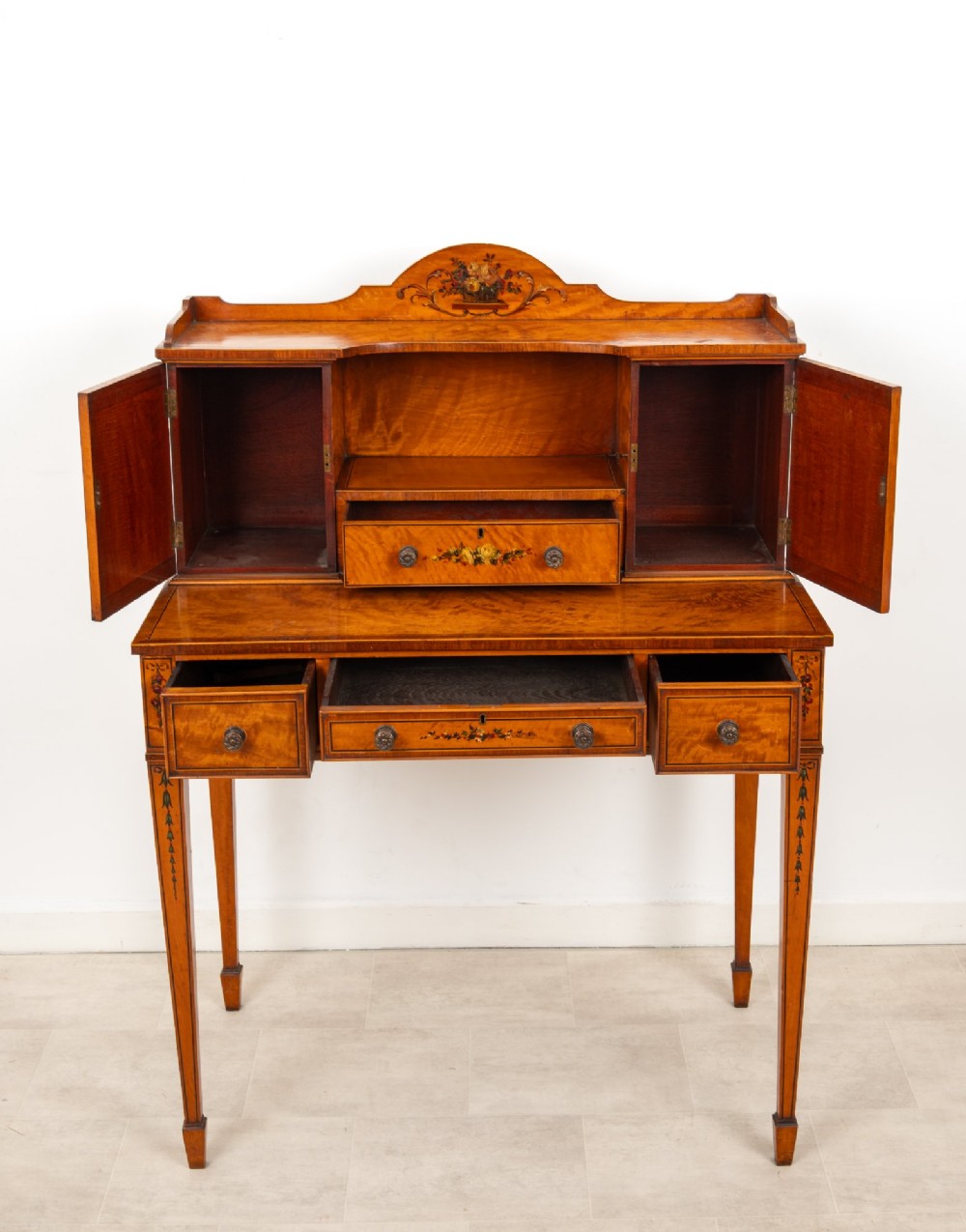 An Edwardian hand-painted satinwood writing desk featuring a raised central cupboard superstructure decorated with painted oval portraits, floral swags, and square tapered legs. View IX