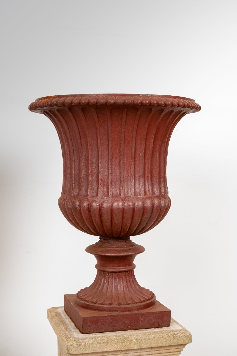 A pair of 19th-century fluted cast iron Campana urns with rust-red finish, elevated on square carved beige stone pedestals. View III