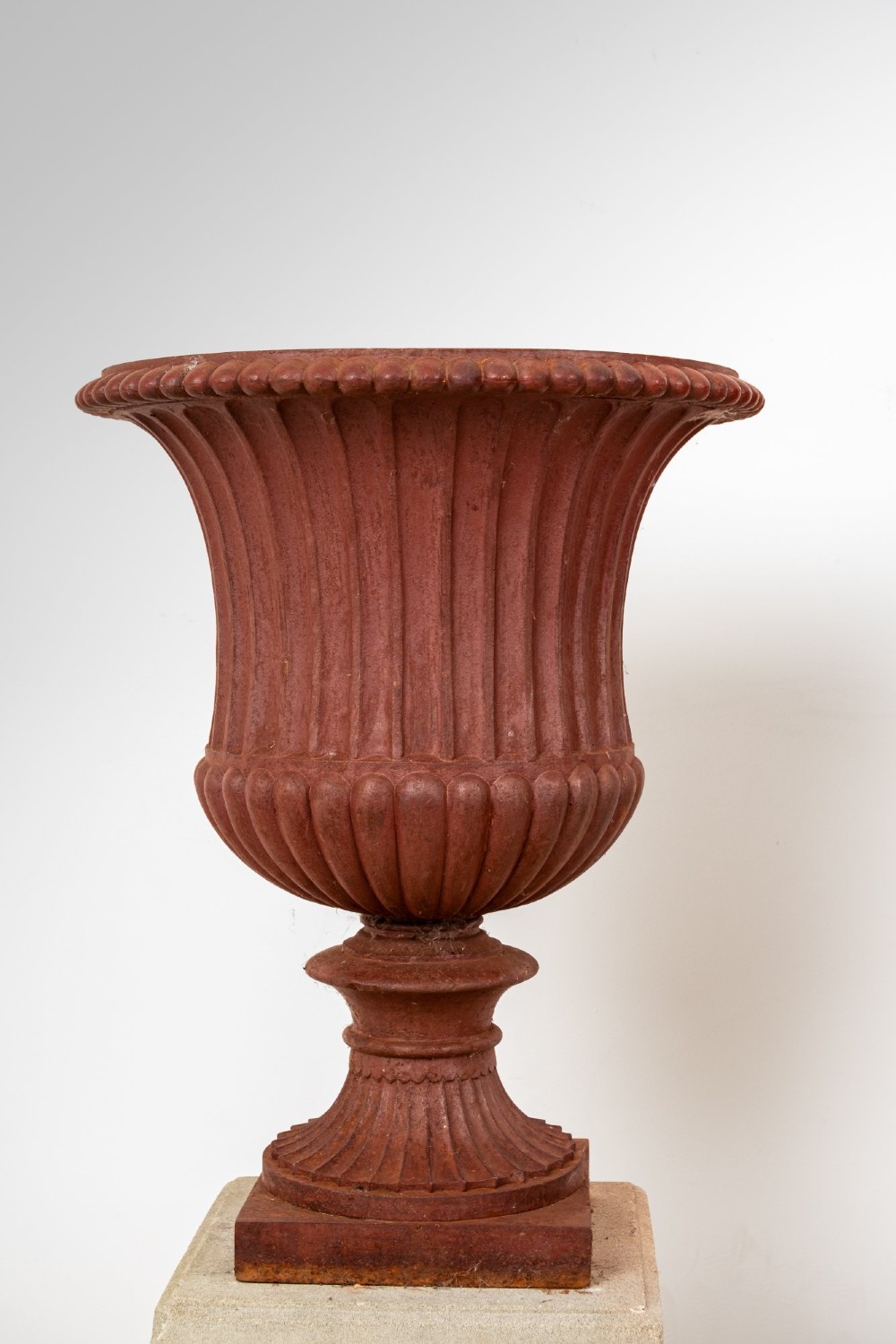 A pair of 19th-century fluted cast iron Campana urns with rust-red finish, elevated on square carved beige stone pedestals. View IV