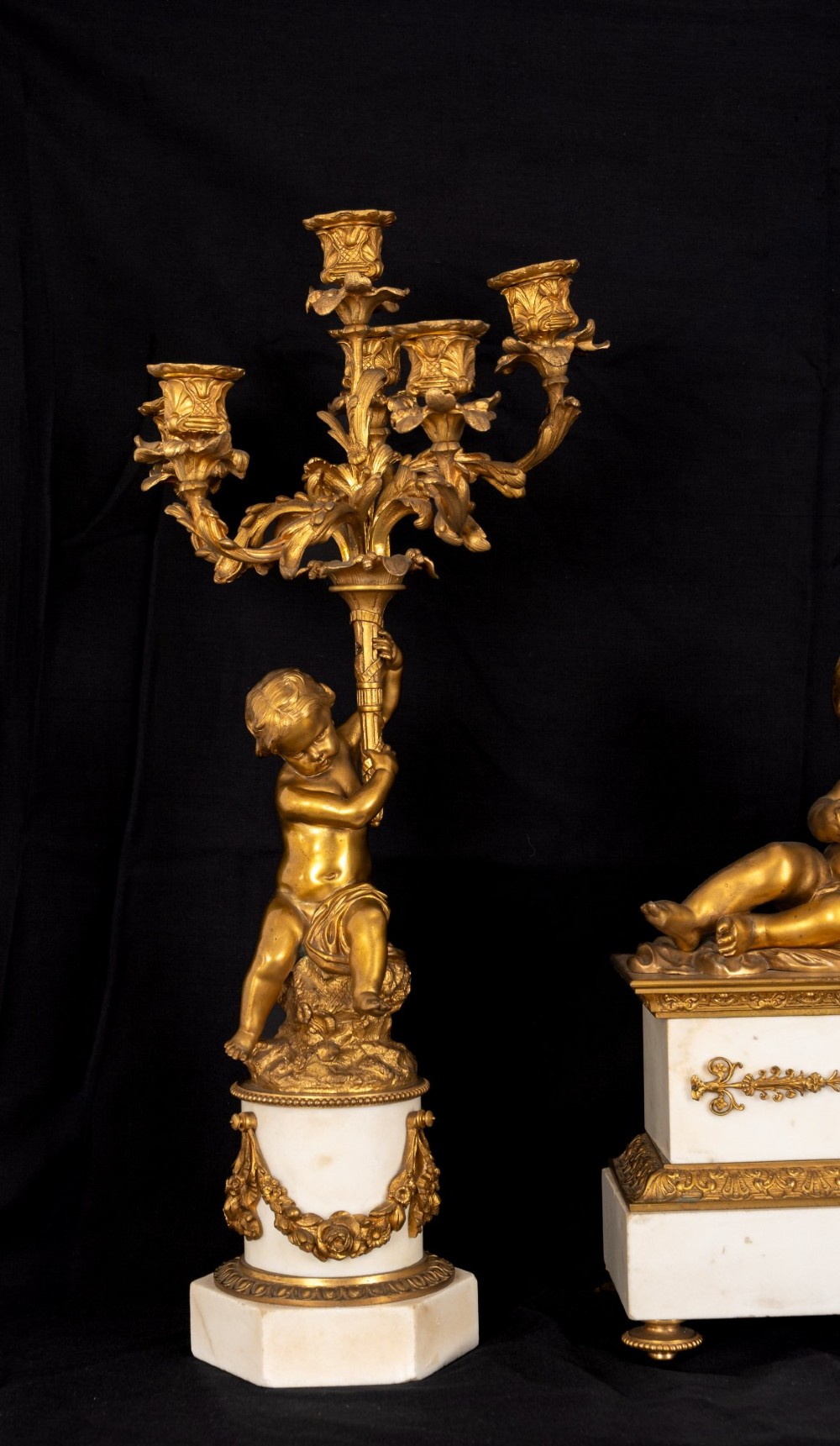 A 19th-century French clock garniture featuring a central white marble and gilt bronze clock topped with two reclining cherub figures, flanked by a pair of matching five-light gilt bronze candelabra supported by cherubs on marble bases. View III