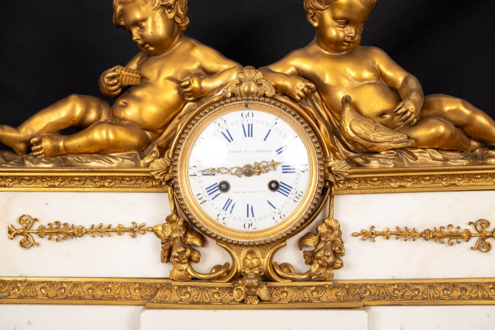 A 19th-century French clock garniture featuring a central white marble and gilt bronze clock topped with two reclining cherub figures, flanked by a pair of matching five-light gilt bronze candelabra supported by cherubs on marble bases. View VII