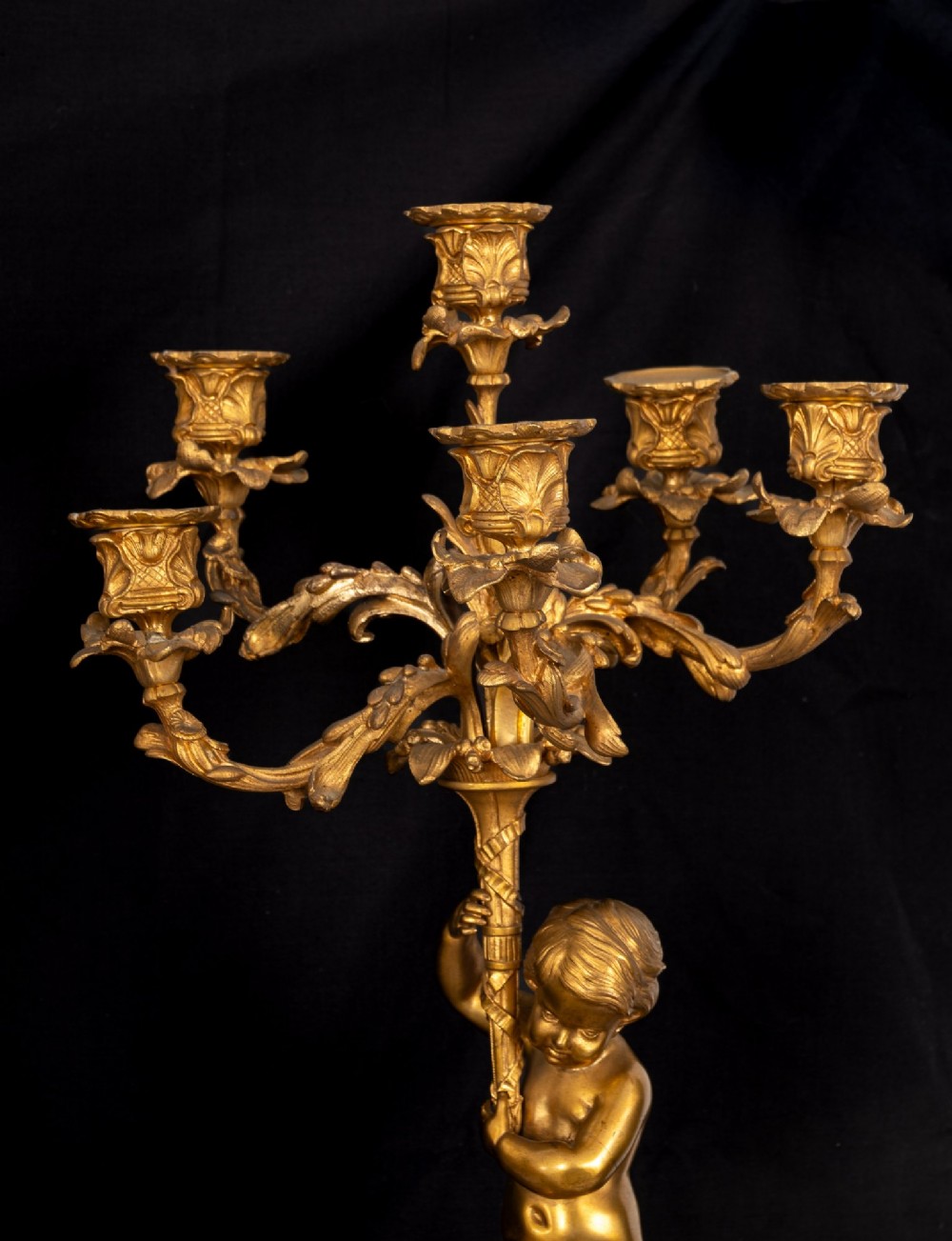 A 19th-century French clock garniture featuring a central white marble and gilt bronze clock topped with two reclining cherub figures, flanked by a pair of matching five-light gilt bronze candelabra supported by cherubs on marble bases. View VIII