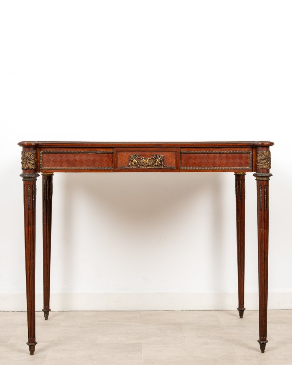 An antique French kingwood writing table featuring geometric parquetry, a single central drawer with ormolu mounts, and four tapered fluted legs.