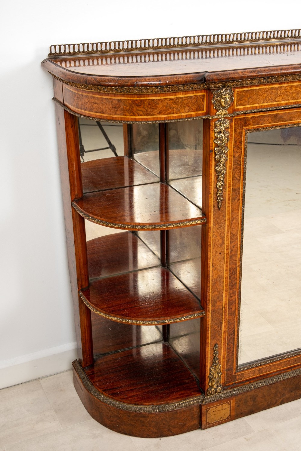 A Victorian burr walnut credenza featuring central mirrored doors, open curved side shelves, and detailed gilt ormolu mounts. View VI