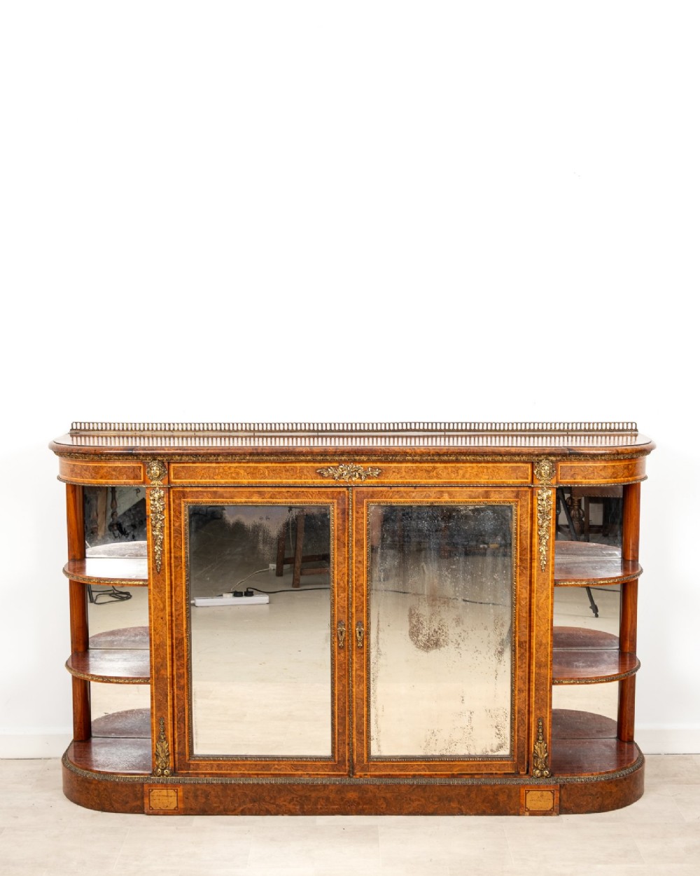 A Victorian burr walnut credenza featuring central mirrored doors, open curved side shelves, and detailed gilt ormolu mounts. View VII