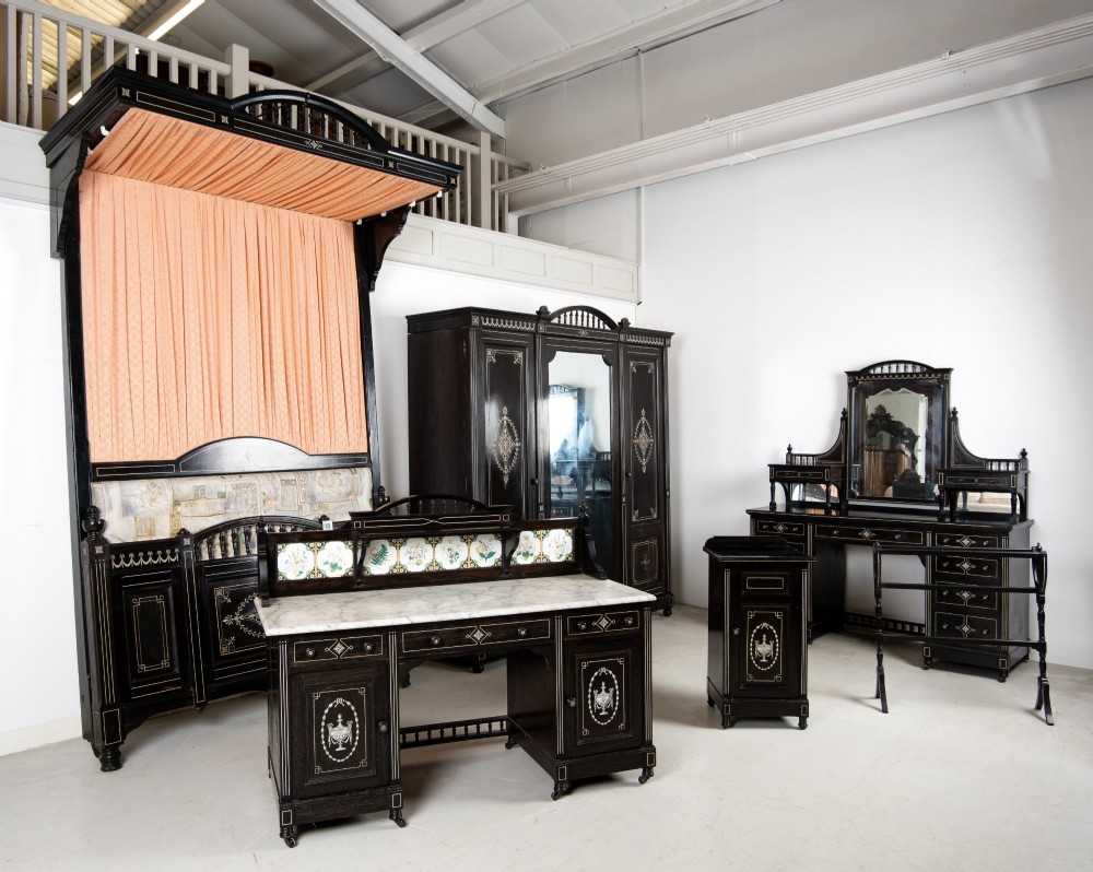 A six-piece late Victorian ebonised bedroom suite featuring bone inlay, comprising a half-tester bed, mirror wardrobe, dressing table, marble-top washstand, nightstand, and towel rail.
