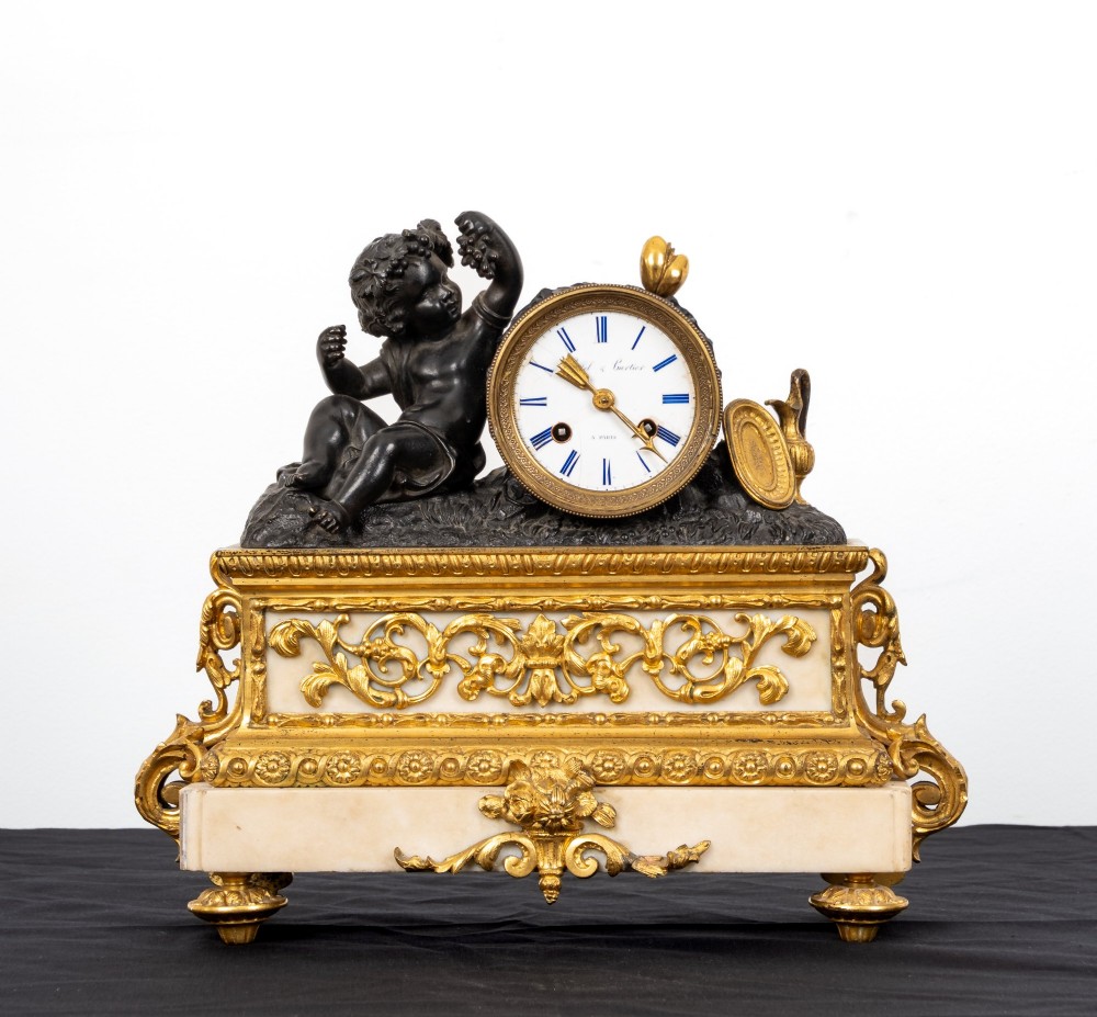A French 19th-century figural mantel clock with a patinated bronze cherub beside a circular white enamel dial on a gilt-bronze and marble base.