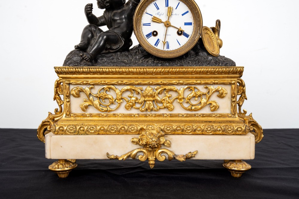 A French 19th-century figural mantel clock with a patinated bronze cherub beside a circular white enamel dial on a gilt-bronze and marble base. View VIII