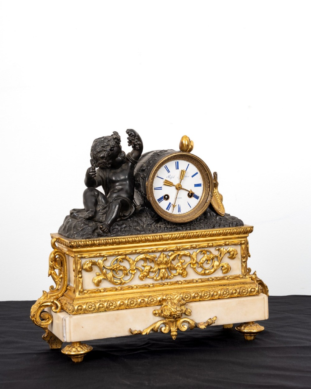 A French 19th-century figural mantel clock with a patinated bronze cherub beside a circular white enamel dial on a gilt-bronze and marble base. View X