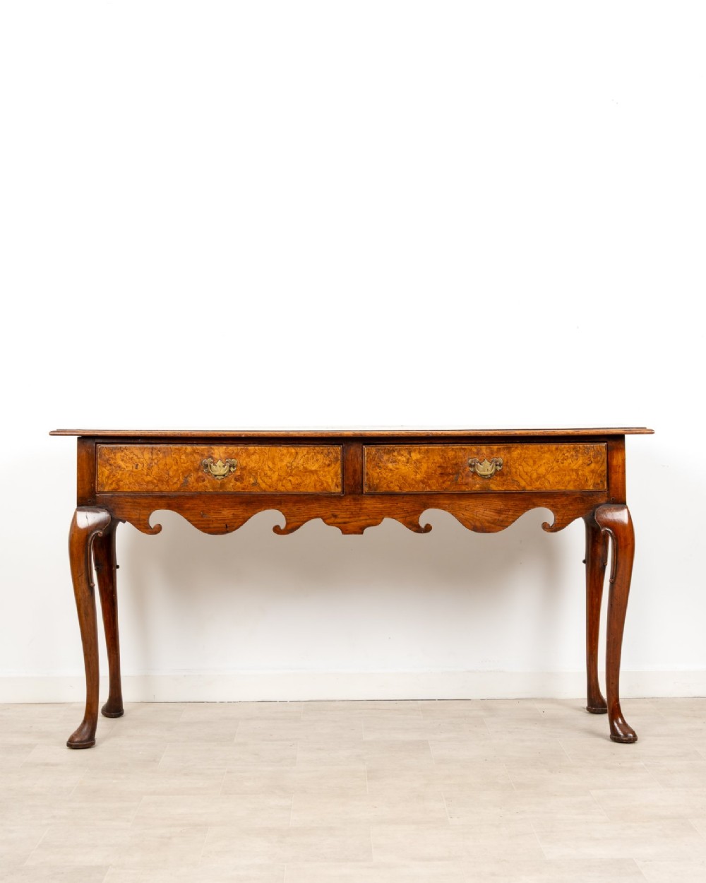 A Queen Anne style burr walnut console table featuring two drawers, a shaped apron, and four slender cabriole legs terminating in pad feet. View II