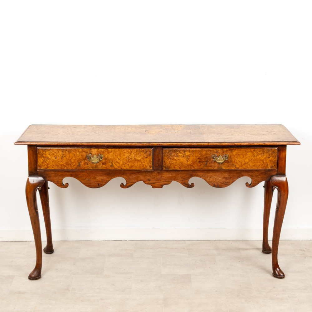 A Queen Anne style burr walnut console table featuring two drawers, a shaped apron, and four slender cabriole legs terminating in pad feet. View III