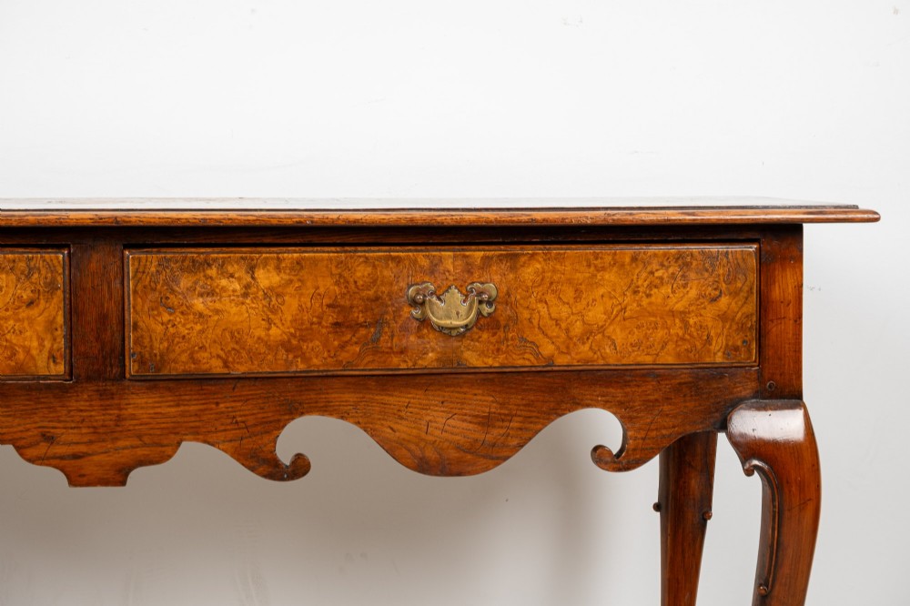 A Queen Anne style burr walnut console table featuring two drawers, a shaped apron, and four slender cabriole legs terminating in pad feet. View IV