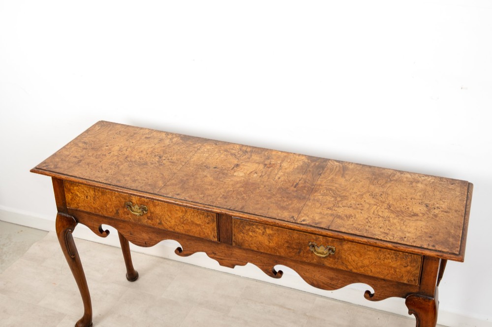 A Queen Anne style burr walnut console table featuring two drawers, a shaped apron, and four slender cabriole legs terminating in pad feet. View V